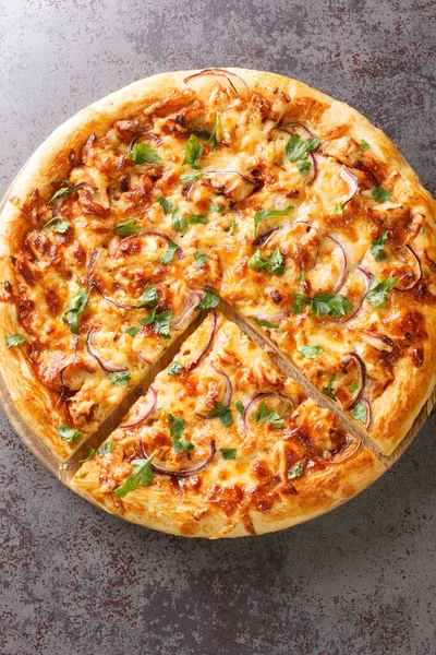 Tasty BBQ Chicken Pizza is a tasty California Pizza with barbecue sauce, cheese and onions closeup on the wooden board on the table. Vertical top view from abov