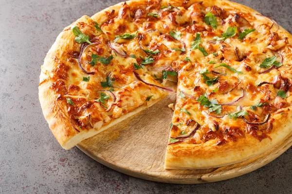 BBQ Chicken Pizza is such a classic with its sweet, tangy, and salty BBQ sauce, bits of juicy chicken, cheese, and savory onions closeup on the wooden board on the table. Horizonta