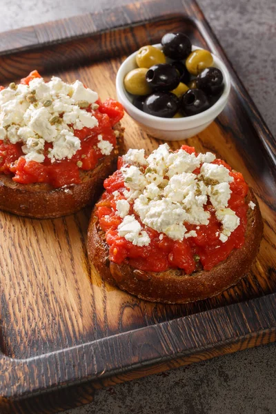 Traditional meze or a light meal on the island of Crete, dakos is often called Greek bruschetta closeup on the wooden board on the table. Vertica
