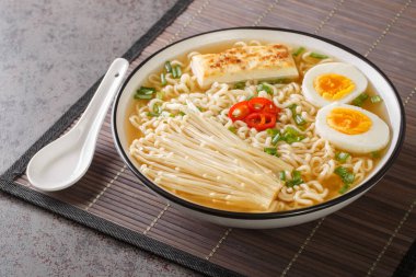 Baharatlı miso ramen çorbası tofu, enoki mantarı, erişte, yeşil soğan ve biberli yakın plan tabakta masada. Yatay