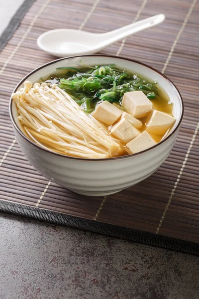 Japanese vegetarian shiro miso soup with tofu, enoki mushrooms, wakame seaweed close-up in a bowl on the table. Vertica