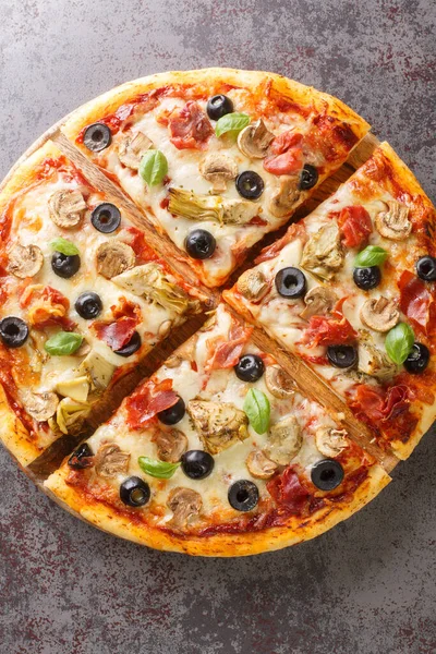 Italian cuisine Pizza capricciosa prepared with mozzarella cheese, ham, mushroom, artichoke, tomato and olive closeup on the wooden board on the table. Vertical top view from abov