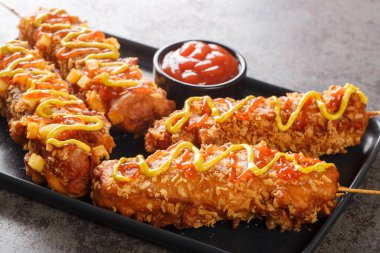 Kore mısırlı sosisli sandviçler, peynir, hamurda kızartılmış patates kızartmaları ve masada şeker, ketçap ve hardalla kaplanmış tabaklar. Yatay