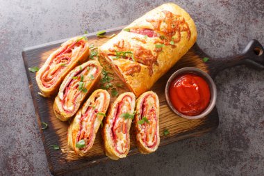 Delicious pizza stromboli roll stuffed with salami sausage and mozzarella cheese close-up on a wooden board on the table. horizontal top view from abov