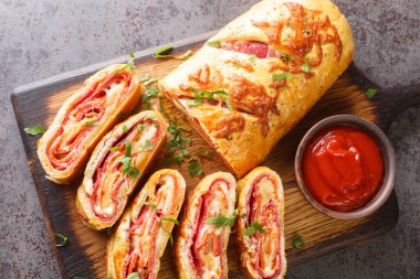 Italian food Pizza roll stromboli with cheese, salami and tomatoes closeup on the wooden board on the table. Horizontal top view from abov