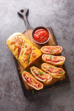 Freshly baked hot pizza stromboli roll with sausage and cheese close-up on a wooden board on the table. Vertical top view from abov