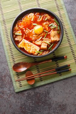 Sundubu jjigae is a Korean stew made with soft tofu, kimchi, pork belly, onion and spices closeup on the bowl on the table. Vertical top view from abov