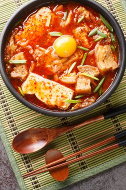 Kimchi Soondubu Jjigae  classic Korean stew features silken tofu in a fiery kimchi broth closeup on the bowl on the table. Vertical top view from abov