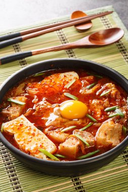 Sundubu Jjigae Spicy Kimchi Soft Tofu Stew closeup on the bowl on the table. Vertica