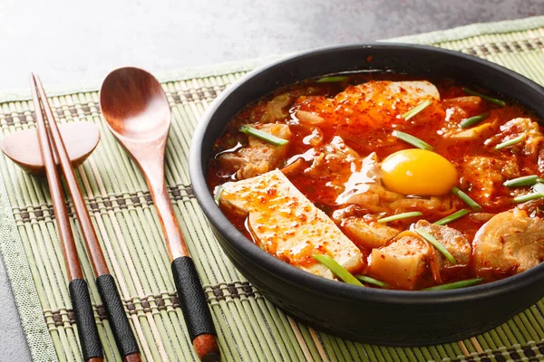 Sundubu Jjigae or soft tofu stew, is a traditional Korean dish made with silky soft uncurdled tofu coated in a spicy and flavorful broth closeup on the bowl on the table. Horizonta