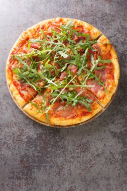 Pizza with prosciutto ham, cheese, tomato sauce and fresh arugula close-up on a wooden board on the table. Vertical top view from abov
