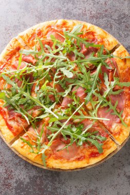 Prosciutto Pizza with cheese, tomato sauce and fresh arugula close-up on a wooden board on the table. Vertical top view from abov