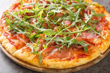 Pizza Prosciutto cooked with tomato sauce, mozzarella, ham, arugula, parmesan close-up on a wooden board on the table. Horizonta