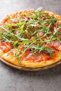 Pizza with prosciutto ham, cheese, tomato sauce and fresh arugula close-up on a wooden board on the table. Vertica