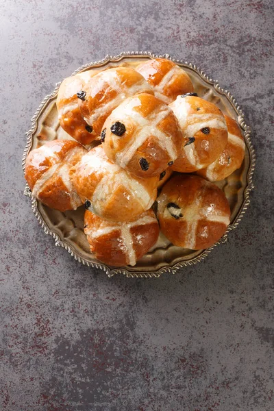 Hot cross buns is a spiced sweet bun usually made with fruit, marked with a cross on the top closeup on the plate on the table. Vertical top view from abov