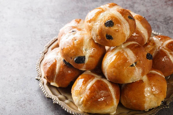 Hot cross bun is a spiced sweet bun made with raisins marked with a cross on the top, and traditionally eaten on Good Friday closeup on the plate on the table. Horizonta