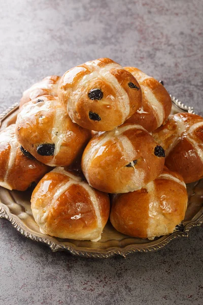 Hot cross buns is a spiced sweet bun usually made with fruit, marked with a cross on the top closeup on the plate on the table. Vertica