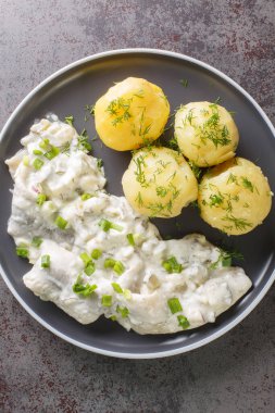 Sahnehering is a German dish with pickled Herrings fillets, apples and onion in a spiced marinade of cream served with boiled potato closeup on the plate on the table. Vertical top view from abov