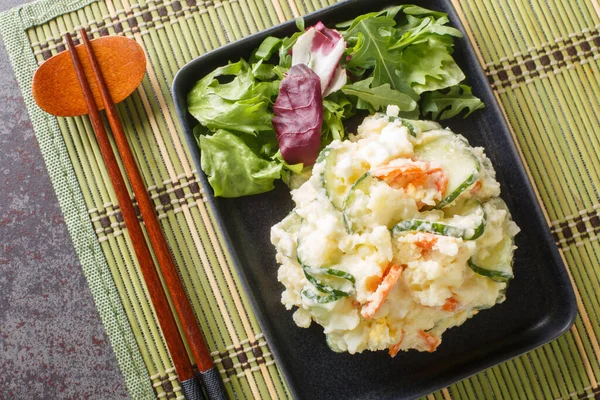 Japanese potato salad is like semi-mashed potatoes mixed with vegetables, egg and mayonnaise close-up in a plate on the table. Horizontal top view from abov