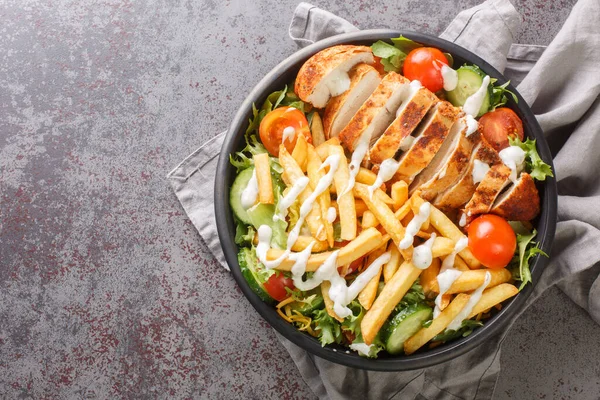 Warm Pittsburgh salad with chicken breast, french fries, vegetables, cheese and lettuce close-up in a bowl on the table. horizontal top view from abov
