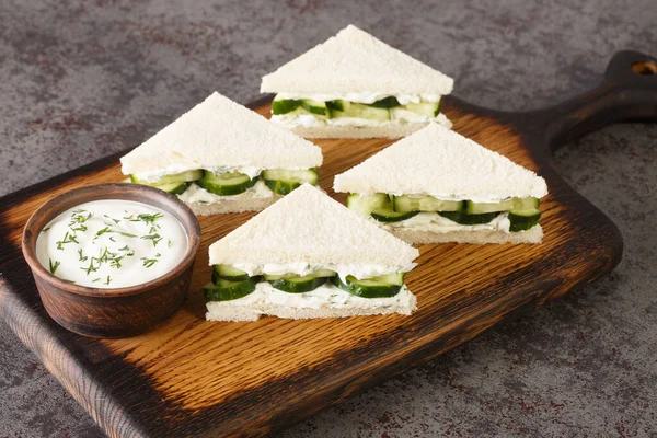 Cucumber Sandwiches are a made with layers of thin cucumbers and fresh herbed cream cheese closeup on the wooden board on the table. Horizonta