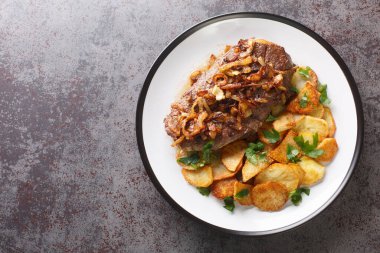 German beef steak Rostbraten with onion and fried potatoes closeup on the plate on the table. Horizontal top view from abov