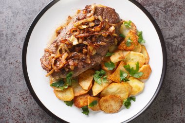Original and Authentic German Zwiebelrostbraten with onion gravy and fried potatoes Bratkartoffeln closeup on the plate on the table. Horizontal top view from abov