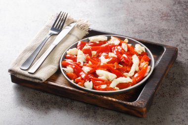 Esgarraet is a typical dish from the Valencian community in Spain it consists of grilled red pepper salad, cured cod, garlic, olive oil closeup on the plate on the wooden board. Horizonta