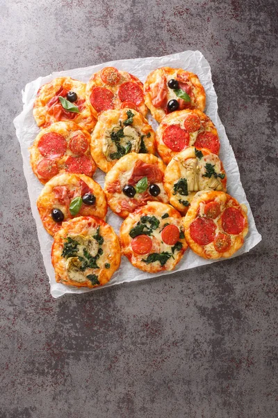 Mix mini pizza or Pizzette with various toppings close-up on parchment on the table. Vertical top view from abov