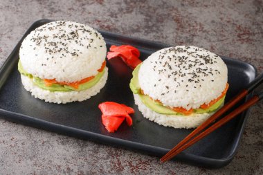 Rice sushi burgers with smoked salmon, avocado, black sesame served on plate with wooden chopsticks close-up. Horizonta