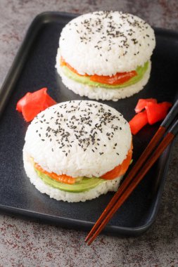 Sushi menu with burger made from rice and smoked salmon, avocado, black sesame and ginger close-up on a plate on the table. Vertica