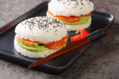 Sushi burger with salmon, avocado and rice close-up on a plate on the table. Horizonta