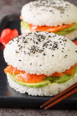 Avocado and Salmon Sushi Burger with black sesame and ginger close-up on a plate on the table. Vertica