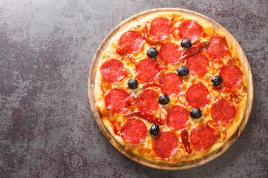 Homemade spicy Pizza Devil with sausage, mozzarella cheese, tomato sauce, chili peppers and black olives close-up on a wooden board on the table. Horizontal top view from abov