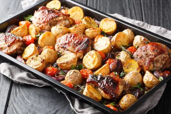 Delicious easy sheet pan Balsamic Chicken with Roasted Potatoes, Red Onion, Tomatoes and fresh herbs close-up on a wooden table. Horizonta