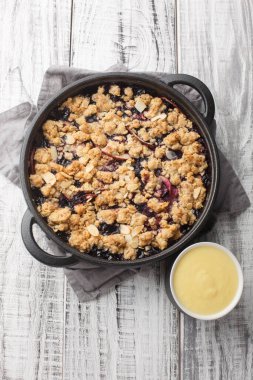 Ev yapımı vanilya soslu İsveç Fruit Crumble Pie Smulpaj 'ı ahşap masaya yakın plan. Yukarıdan dikey üst görünüm