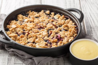 Elma ve yaban mersiniyle pişirilmiş meyveli çörekler vanilya sosuyla servis edilir. Masanın üzerinde yakın plan bir tavada. Yatay