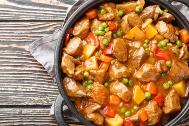 Patatesli, havuçlu, domatesli, yeşil bezelyeli, soğanlı ve baharatlı yavaş pişmiş biftek, ahşap bir masada kızartma tavasında. Yukarıdan yatay üst görünüm