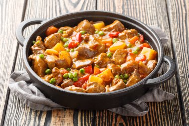 Patatesle, havuçla, domatesle, yeşil bezelyeyle, kendi meyve sularında, ahşap bir masadaki bir tencerede soğanla pişirilmiş baharatlı biftek. Yatay