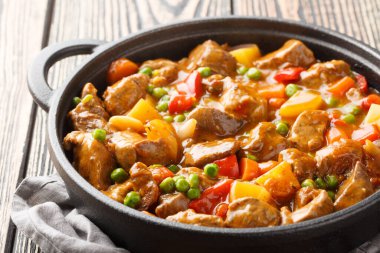 Patatesli, havuçlu, domatesli, yeşil bezelyeli, baharatlı soslu soğanlı, ahşap bir masada kızartma tavasında. Yatay