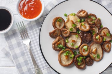 İştah açıcı kızarmış shiitake mantarı ve yeşil soğan. Masadaki beyaz tabakta yakın plan. Yukarıdan yatay üst görünüm