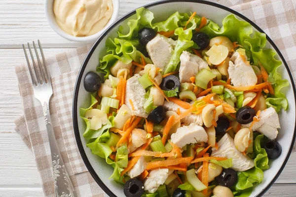 stock image Healthy diet salad with chicken, mushrooms, carrots, celery, olives, cheese and lettuce close-up in a bowl on a wooden table. Horizontal top view from abov