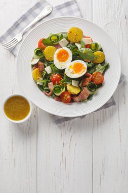 Masanın üzerinde roka, ıspanak, patates, pastırma, domates, peynir ve rafadan yumurta ile taze köylü salatası. Yukarıdan dikey üst görünüm