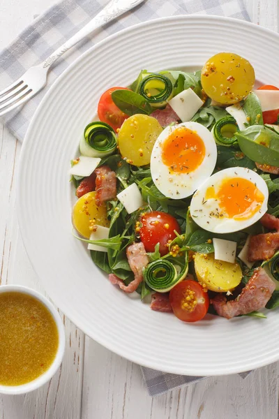 stock image Summer fresh salad with potatoes, tomatoes, bacon, arugula, zucchini, cheese and soft-boiled eggs close-up on a plate on the table. Vertical top view from abov