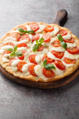 Masanın üzerinde mozarella, domates ve fesleğen yapraklı klasik caprese pizzası. Dikey