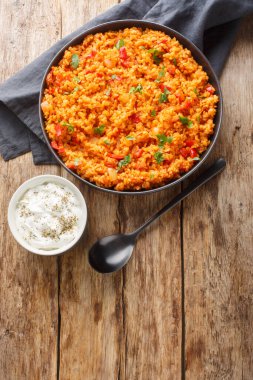 Bulgur pilav mı? Tahta bir masadaki bir kasede soğan, yeşil biber, domates ve çeşitli baharatlarla tatlandırılmış besleyici bir Türk pilavı. Yukarıdan dikey üst görünüm