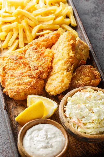 Fish Fry is accompanied by coleslaw, French fries, tartar sauce closeup on the wooden board on the table. Vertica