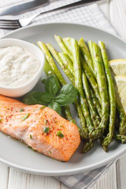 Masadaki tabakta tartar soslu kuşkonmaz ile servis edilmiş fırında somon filetosu. Dikey