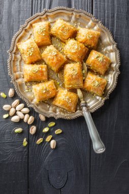 Ballı ve şekerli tereyağlı Türk Baklava 'sı ahşap masadaki tabağa yakın hamur katmanları arasına yerleştirilmiş taze fıstıklı yumuşak puf böreği. Yukarıdan dikey üst görünüm