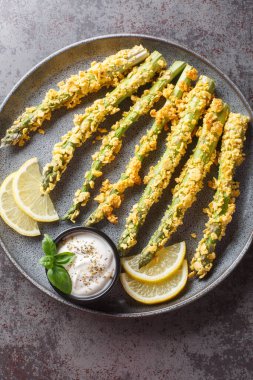 Panko ekmek kırıntıları ve sosla servis edilen parmesan peynirli kuşkonmaz ve masada limonata. Yukarıdan dikey üst görünüm